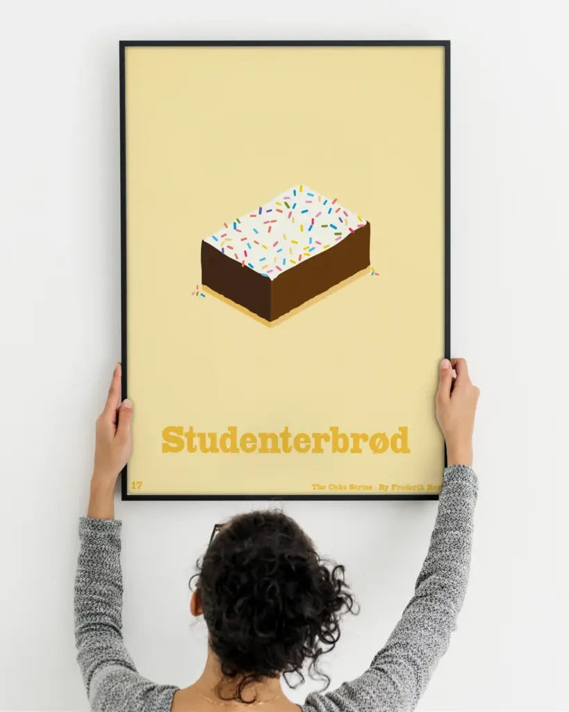 A mockup of a woman holding a framed poster to a wall, the poster is of a danish pastry named "Studenterbrød"